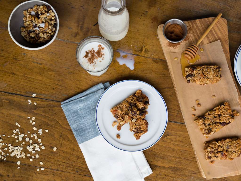 Aerial shot of granola-textured breakfast bars with various ingredients neatly placed around it, including a glass of milk on a wooden tabletop.