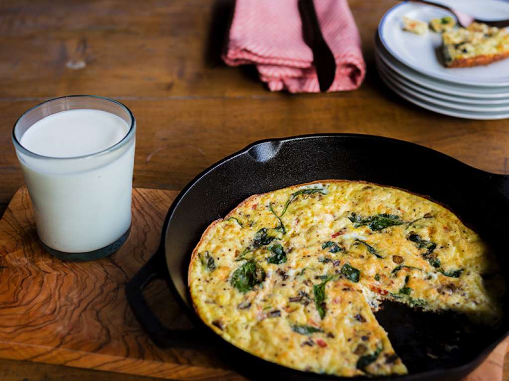 Aerial shot of a veggie frittata in a cast iron skillet with a glass of milk next to it.